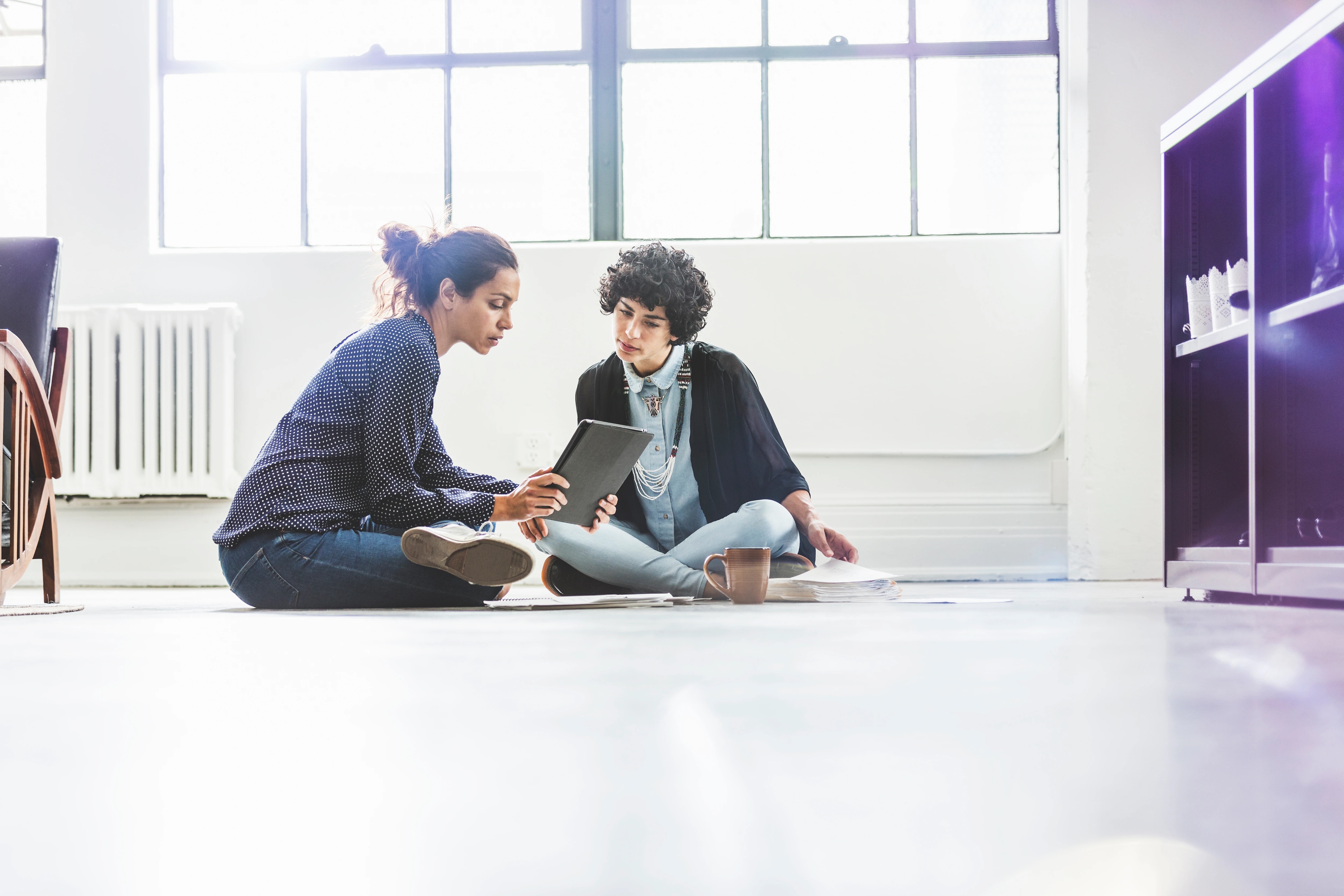 Two women looking at tablet; sitting on floor