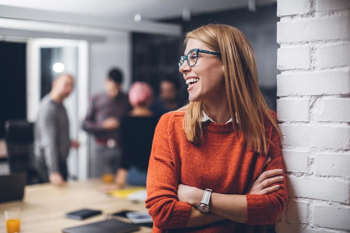 Woman in office laughing and leaning against wall