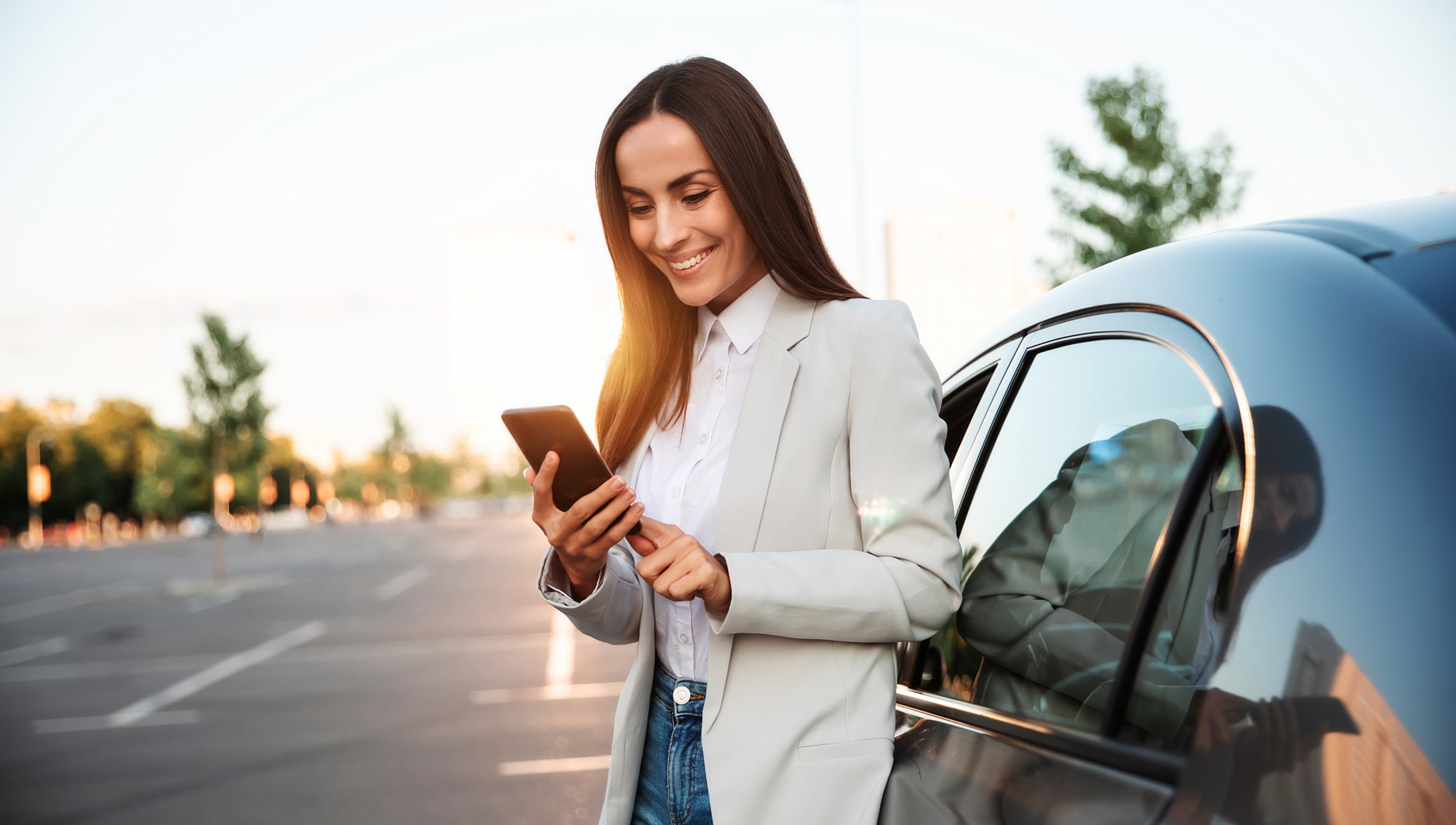 Woman with phone leaning against car