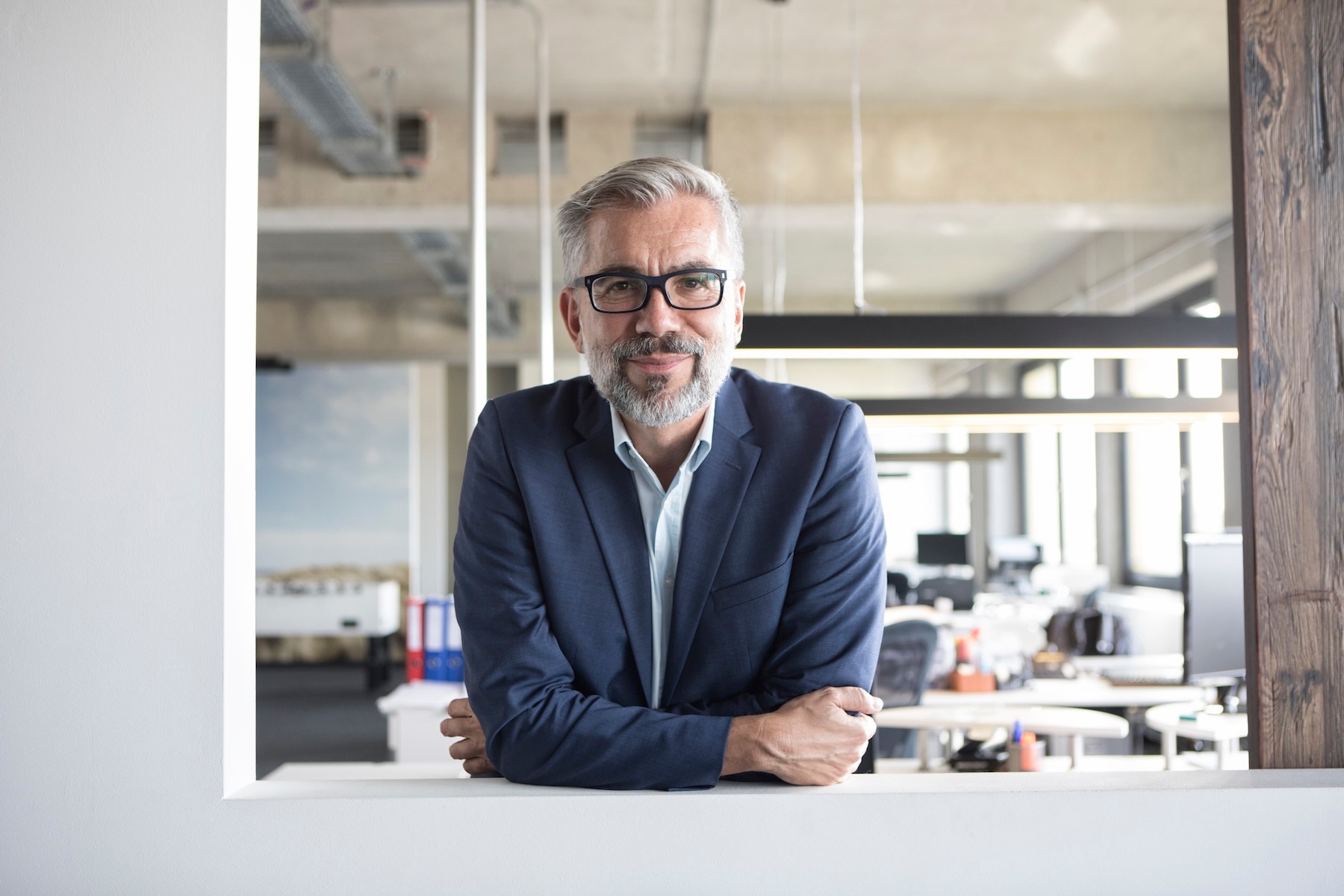 Man with grey hair and glasses, smiling and crossing arms